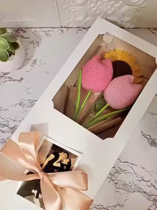 Una caja de regalo con dos tulipanes y un girasol tejidos a crochet, con un lazo y una foto polaroid personalizable
