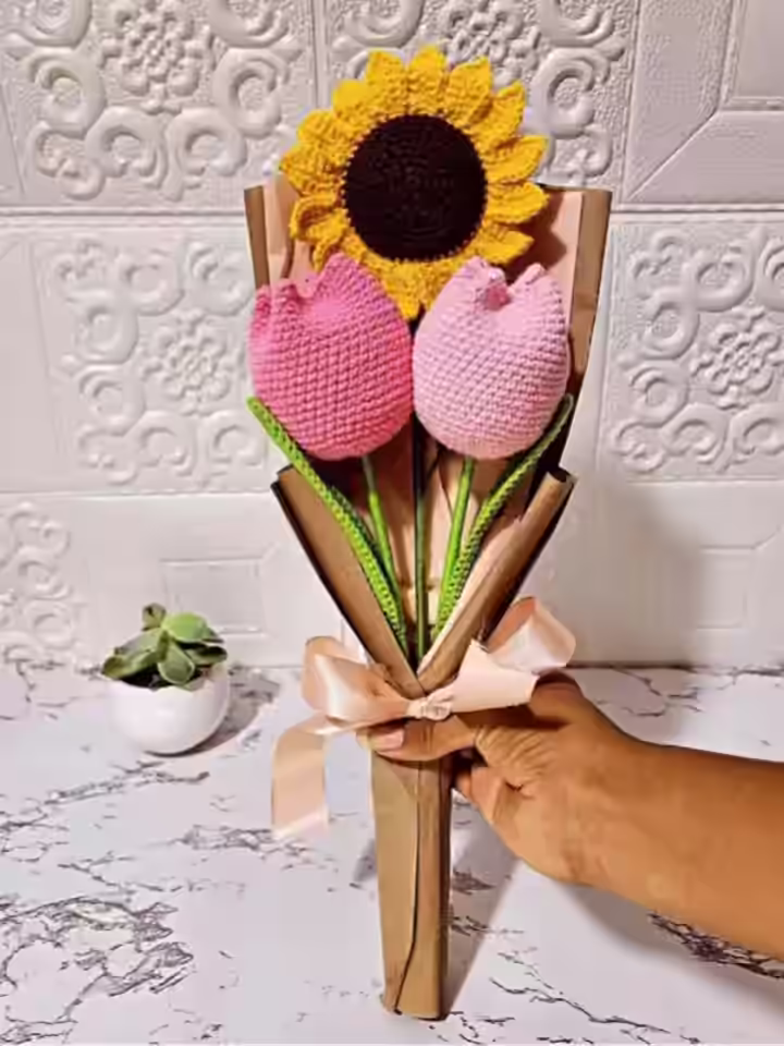 Un ramo de flores tejidas a crochet de dos tulipanes y un girasol sostenido con una mano